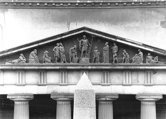 Pediment above the tops of four columns showing twelve disciples; Christ in centre with raised right arm and cross on pole in left hand 